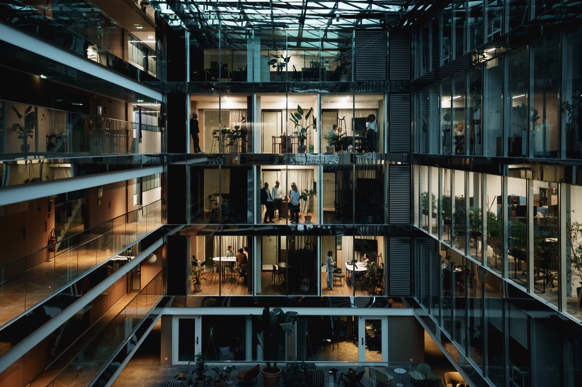 A lit atrium at night, each room holding a different group of people.